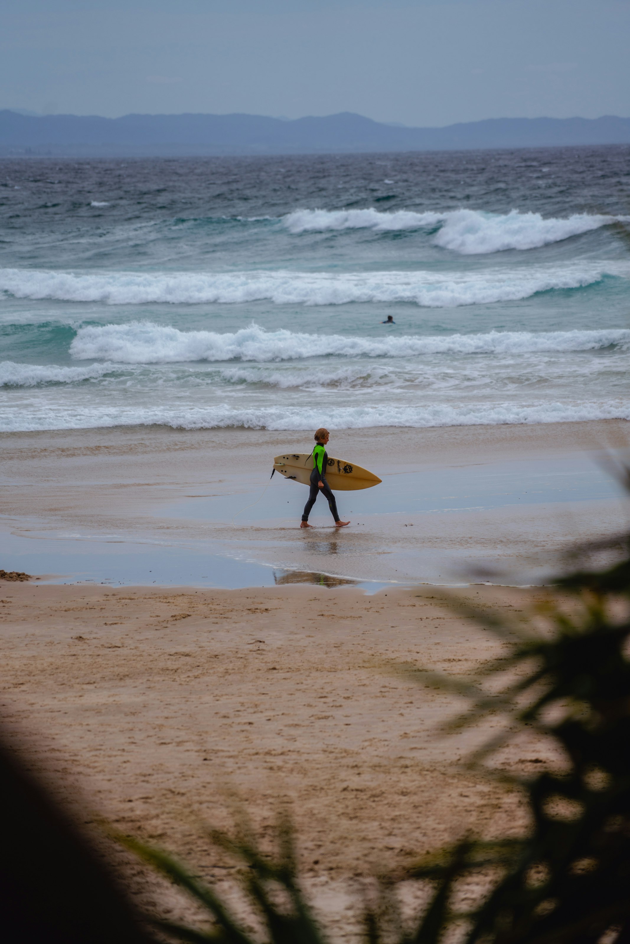 man in green shirt holding yellow surfboard walking on beach during daytime